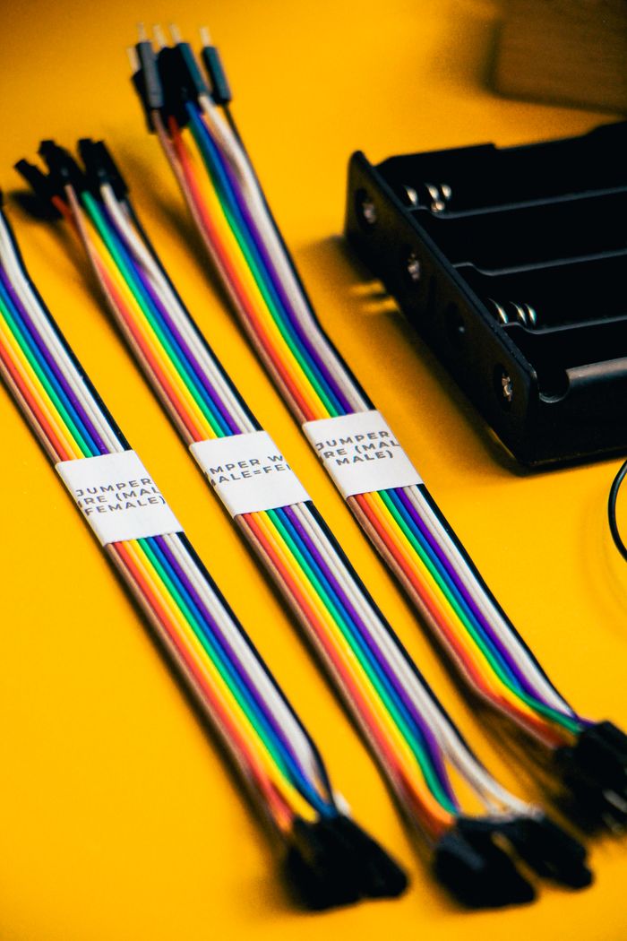 Vibrant close-up of rainbow-colored jumper wires and a battery holder on a yellow background.